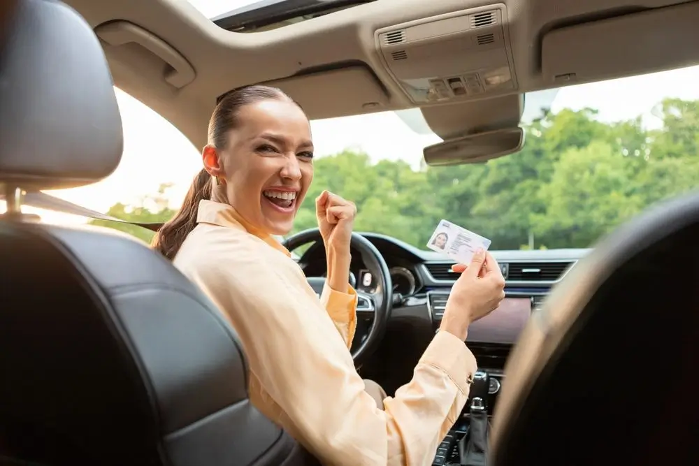 driving school. Overjoyed European lady sitting in her own car and holding new driver license, celebrating driving school finish, sitting inside of vehicle.